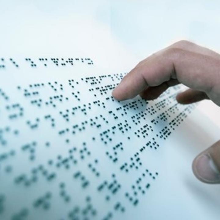 A person's hand reading Braille on Braille Paper