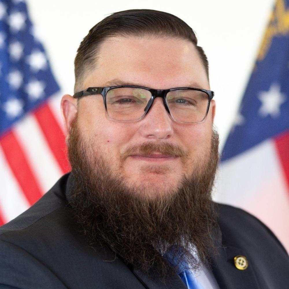 Jeff Allen with black-rimmed glasses smiling in a suit