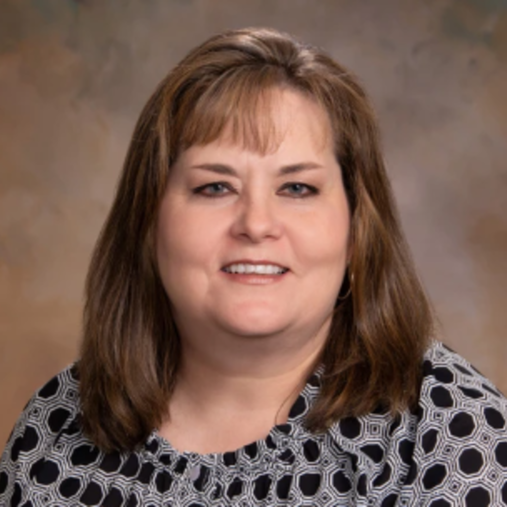 White woman with brown shoulder length hair wearing a black and white blouse