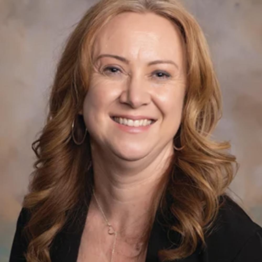 A headshot photo of a woman that is smiling wearing a black blazer.