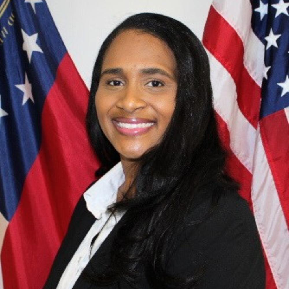 A woman smiling in front of two flags. 