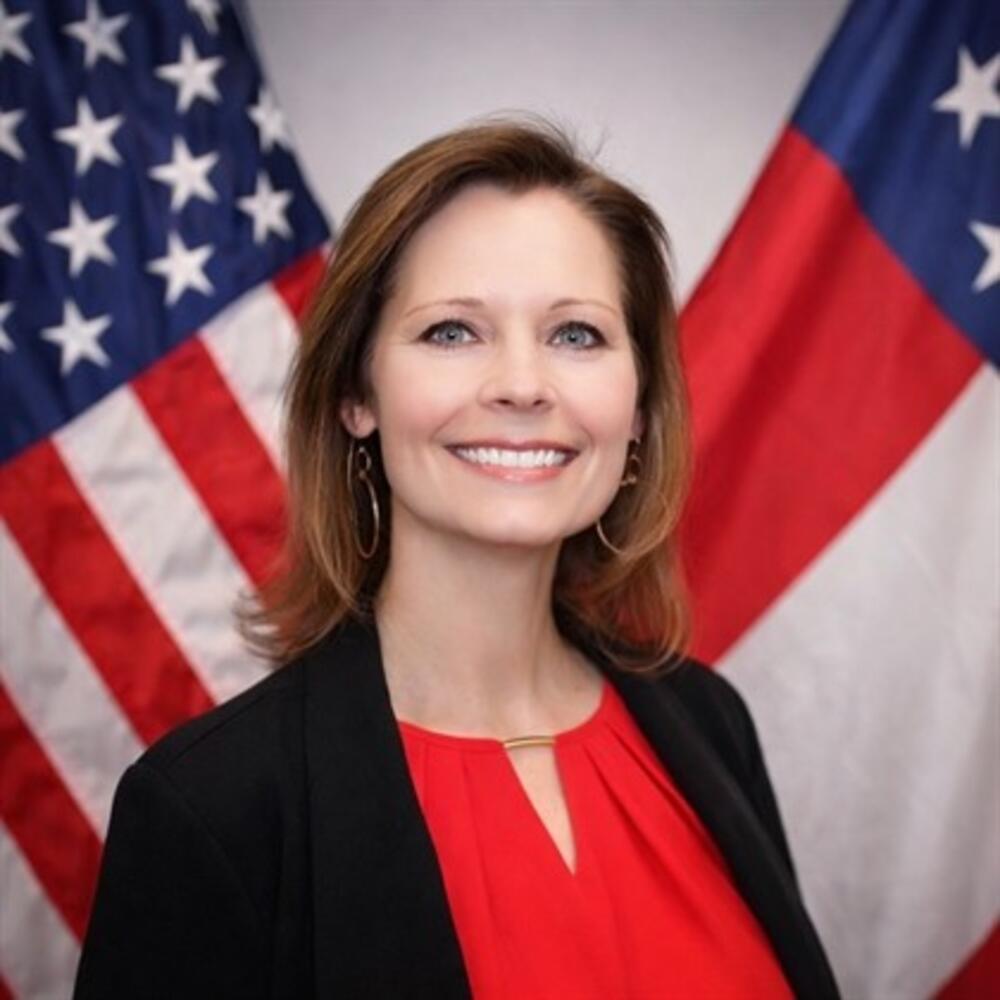 Woman with reddish-brown hair wearing a red shirt with a black jacket