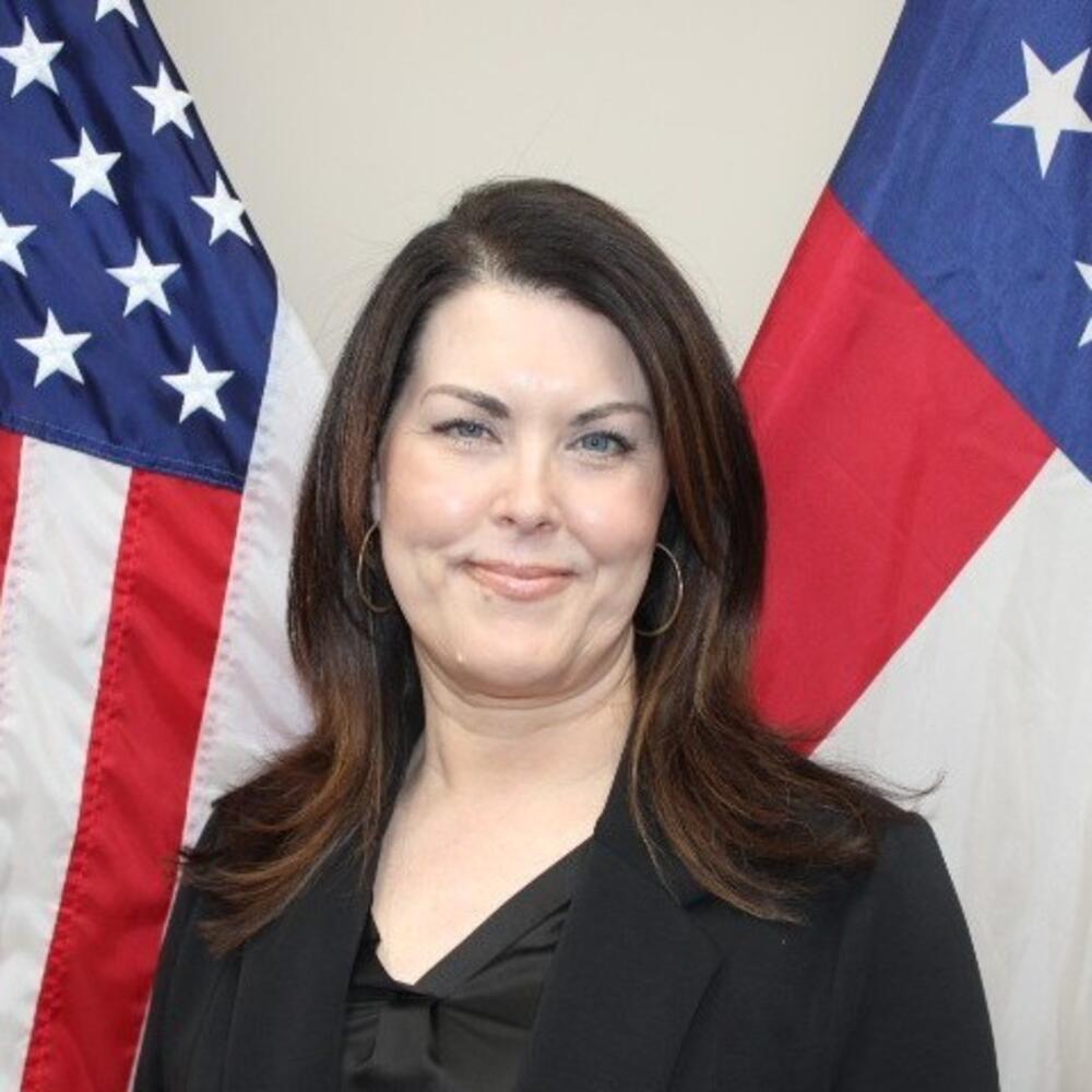 Woman with dark shoulder length hair wearing a black blouse and black jacket