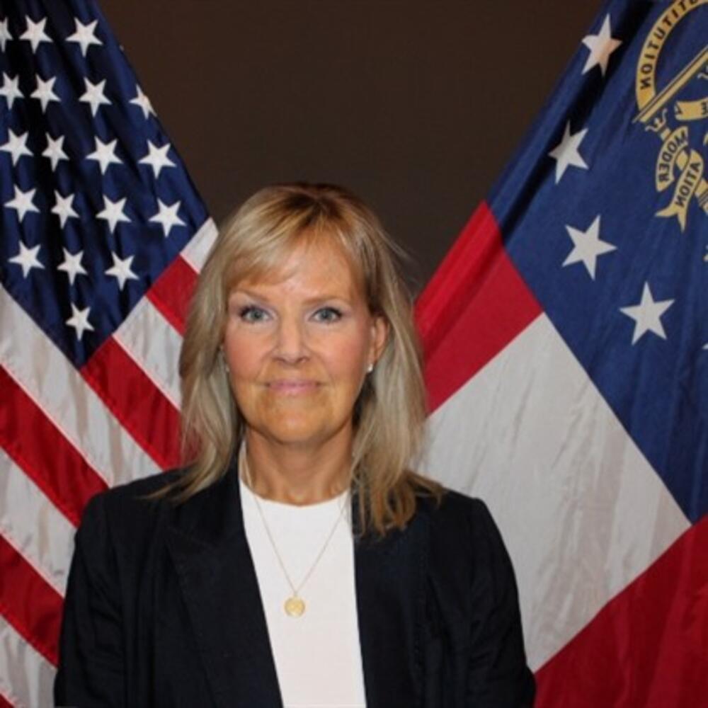 Woman with blonde shoulder length hair wearing a white shirt and blue jacket