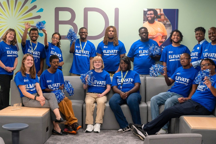 A group photo of students wearing blue shirts and have black and white pom poms in their hands. 