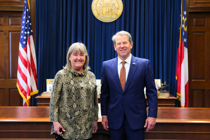 In the Governor office and a woman and man standing in front of two flags. 