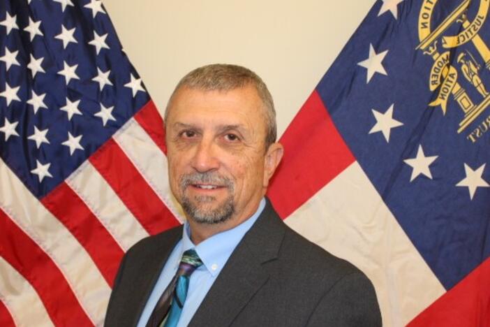 A man wearing a black suit standing behind two flags. 