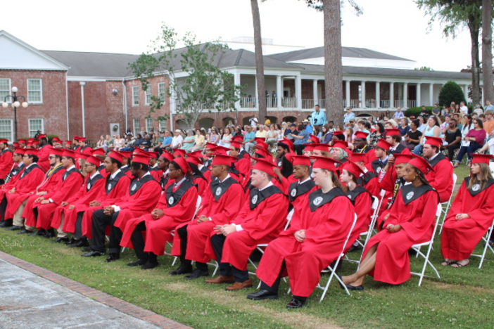 A group of RWS graduates sitting down wearing red graduation gown and cap. 