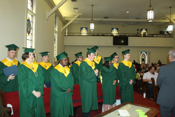 CSC graduates standing up and wearing green graduation gown and cap. 