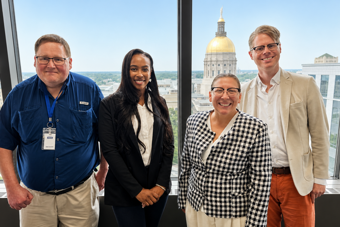 Four people standing behind a window has the capitol building in the background. 