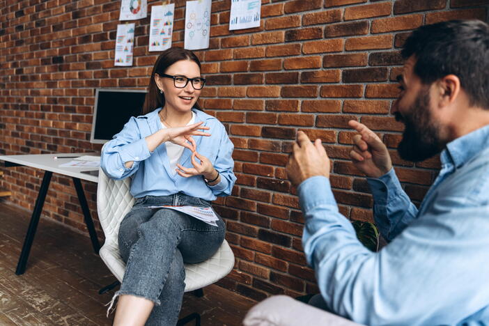 Two people that are sitting down and are doing sign language behind a brick wall. 